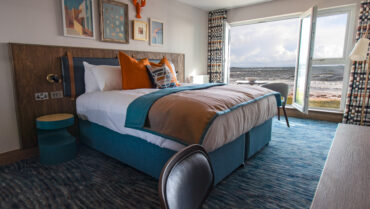 Image of king sized bed with a window behind it over looking the sea.
