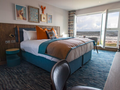 Image of king sized bed with a window behind it over looking the sea.
